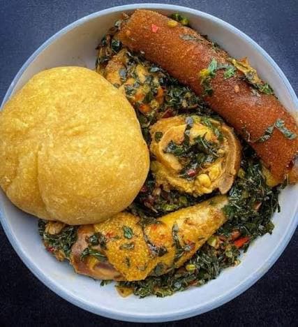 A ball of eba on a plate beside a bowl of vegetable soup with fish